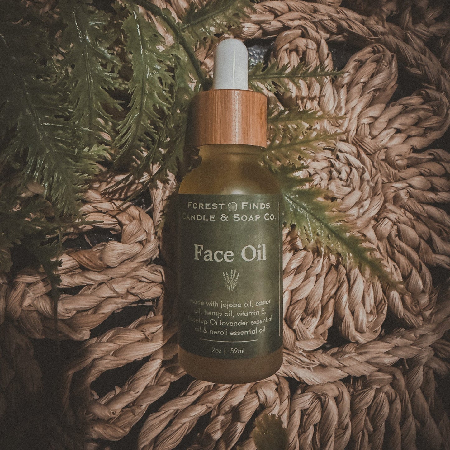Face oil bottle with dropper on a textured surface with green leaves