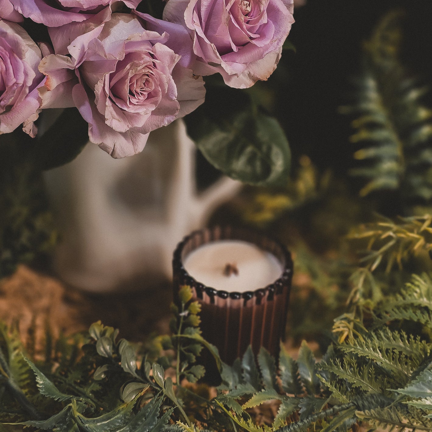 Bouquet of pink roses with a candle and greenery on a dark background