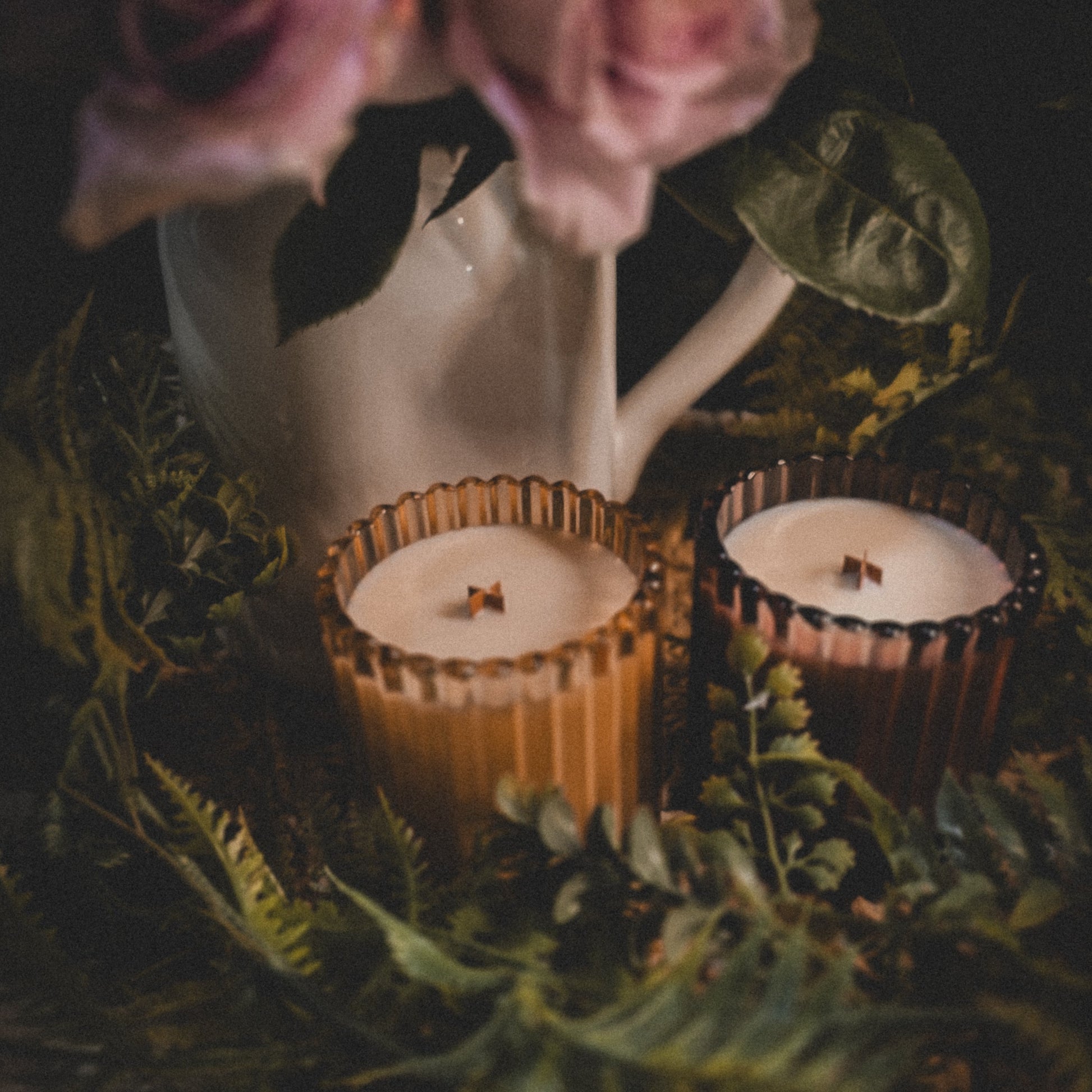 Two small candles in rustic holders with a bouquet of flowers in the background.