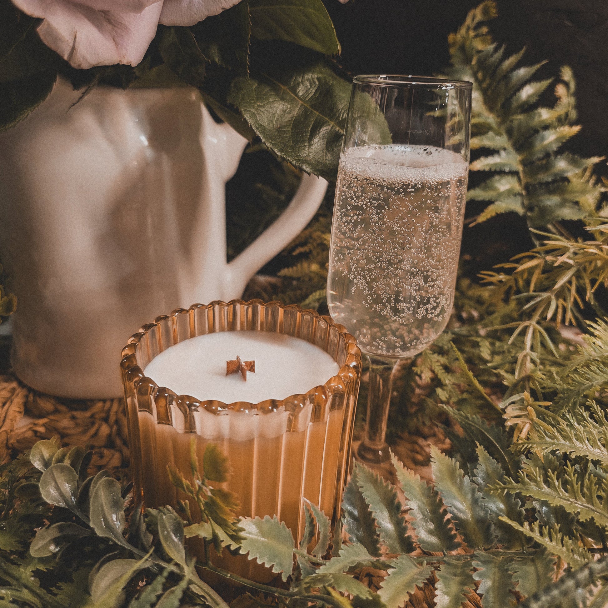 Candle in a glass holder with a glass of champagne and pink roses on a dark background