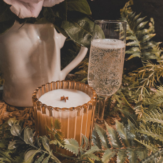 Candle in a glass holder with a glass of champagne and pink roses on a dark background