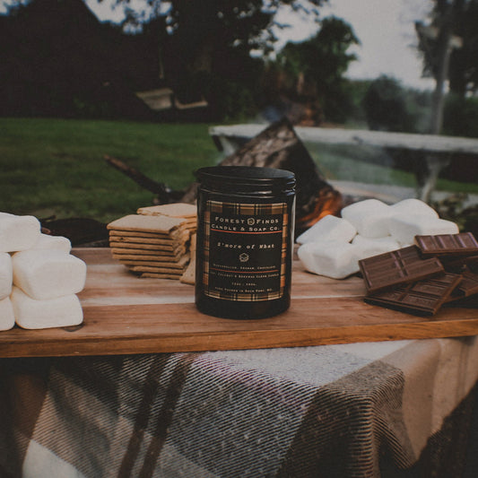 Outdoor setting with marshmallows, graham crackers, chocolate bars, and a jar of marshmallow cream on a wooden board.